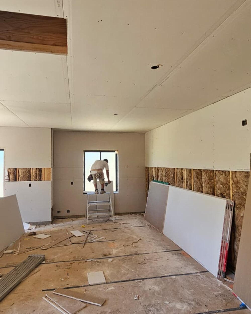 Worker hanging drywall panels near a window